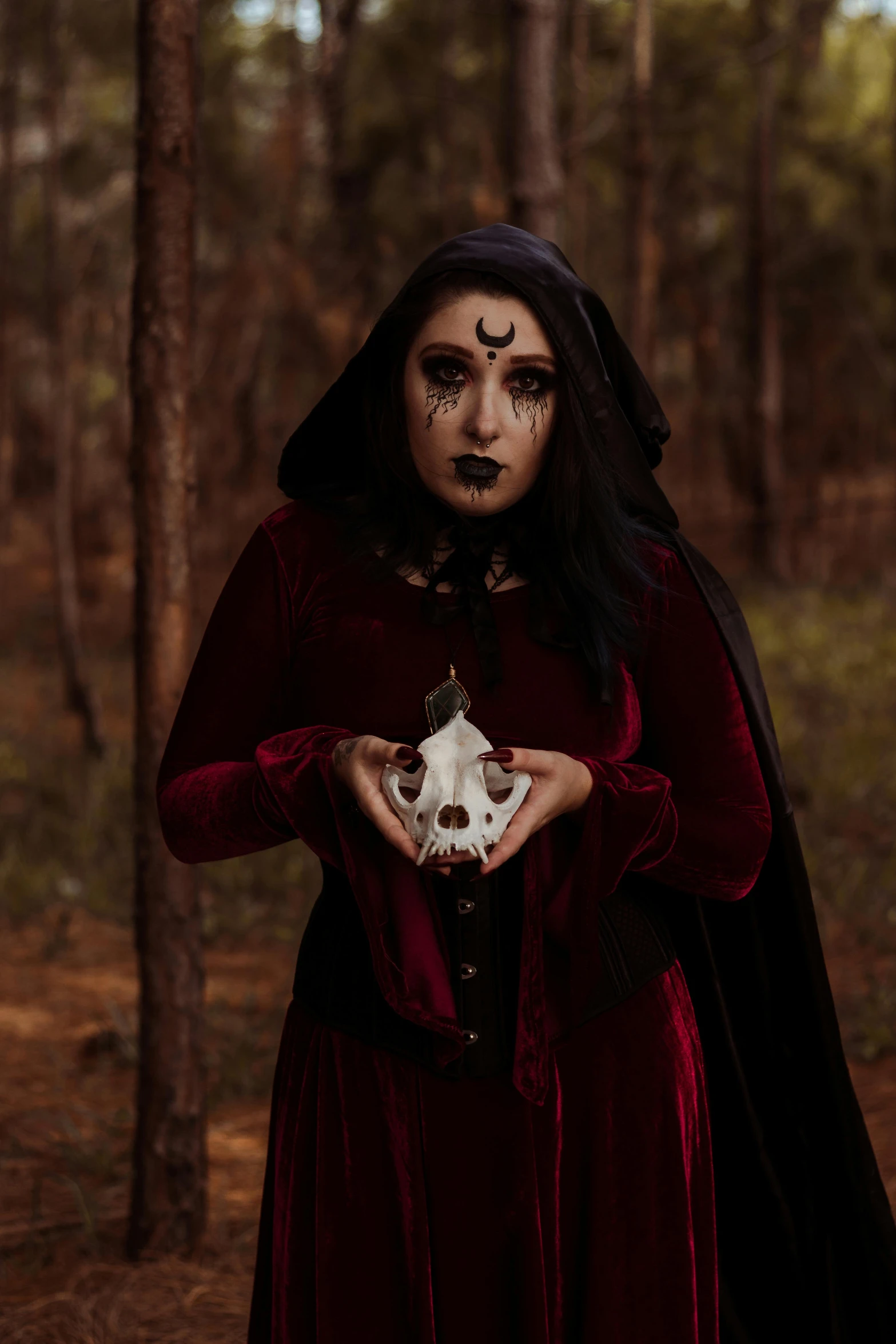 a girl in a gothic costume standing in a forest holding a white skull