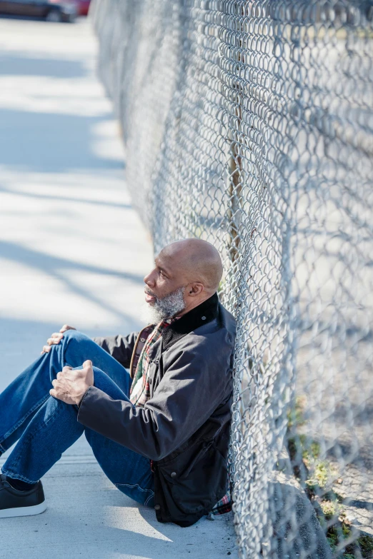 an elderly black man sitting against a fence