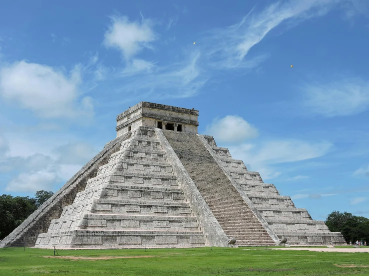 an ancient pyramid is on the grass near a blue sky