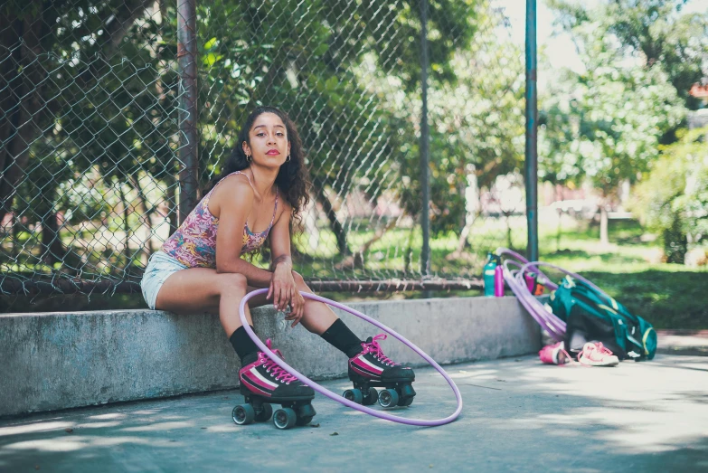 girl with purple hoops sitting on concrete with skates next to fence