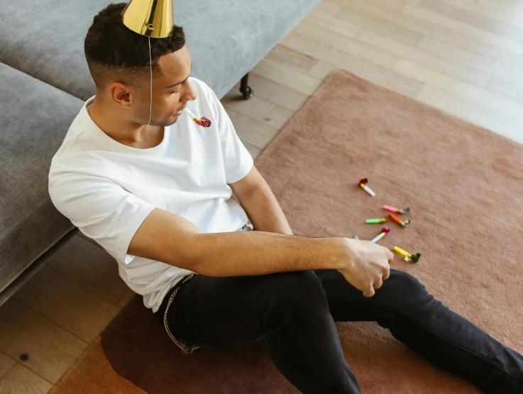 the man wearing a party hat smiles while sitting on the floor