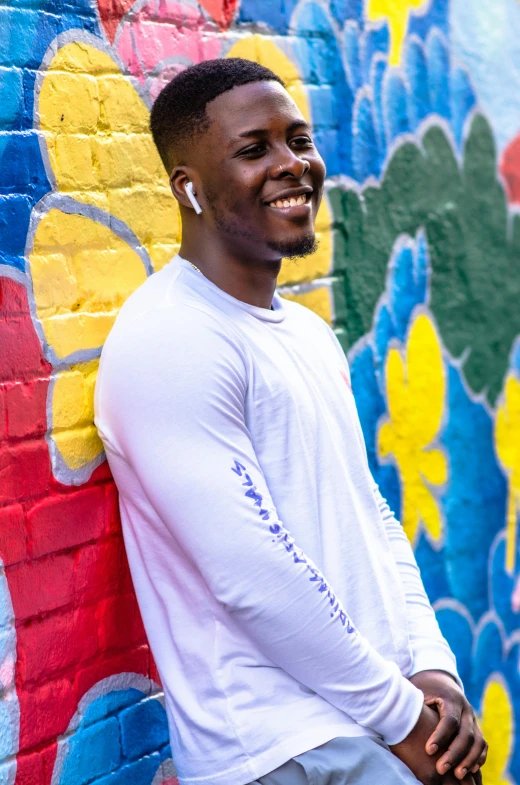 a smiling man leaning against a wall with a flower pattern painted on it