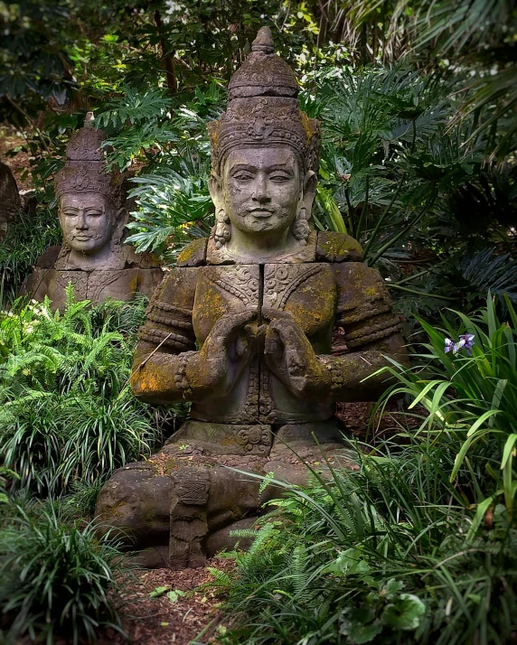 a statue of three seated buddhas surrounded by lush vegetation