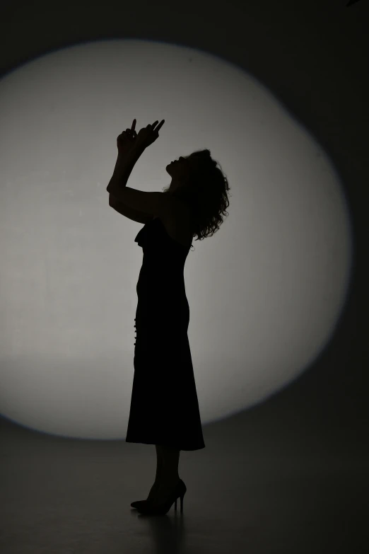 the silhouette of a woman in a short dress holding her hand up