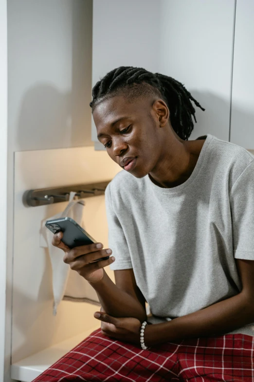 a man with dreadlocks sitting on the toilet using his cell phone