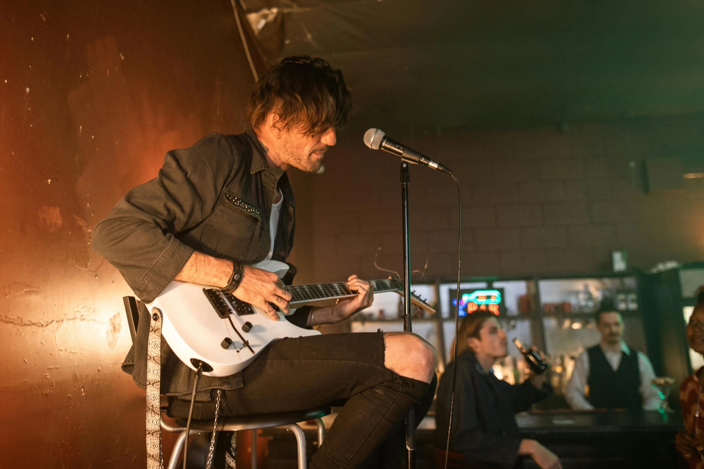 a man holding a guitar and sitting in front of a microphone