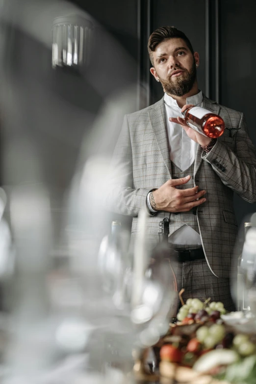 a man in a suit stands at a table with glasses and holds a small pepper shaker