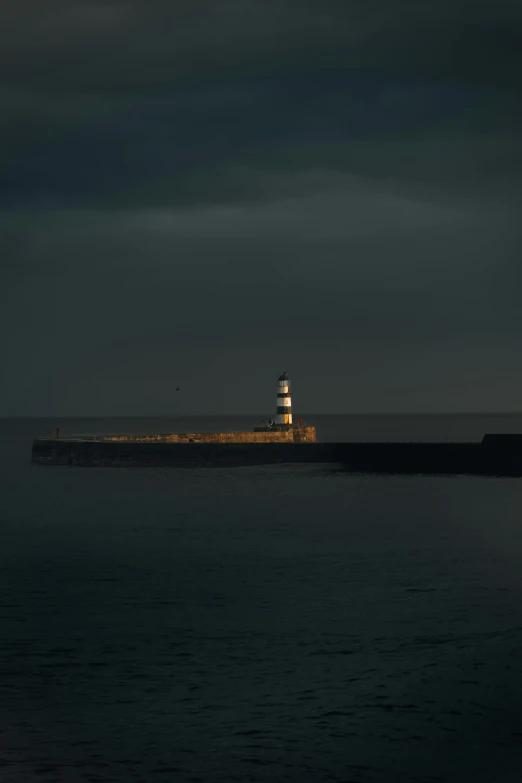 a lighthouse at dusk by the ocean under a cloudy sky