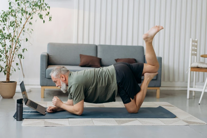 a man on a rug with a laptop in his hand, stretching his arms