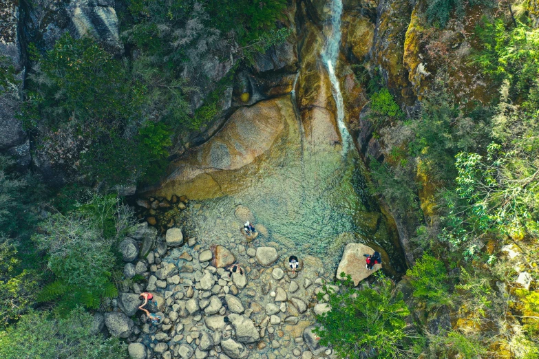 two people sitting on rocks under a small waterfall