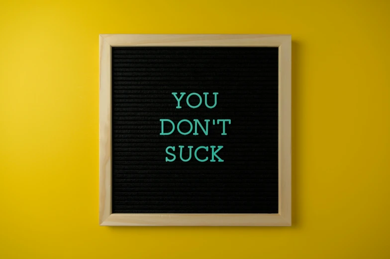 a black sign on yellow wall that says you don't suck