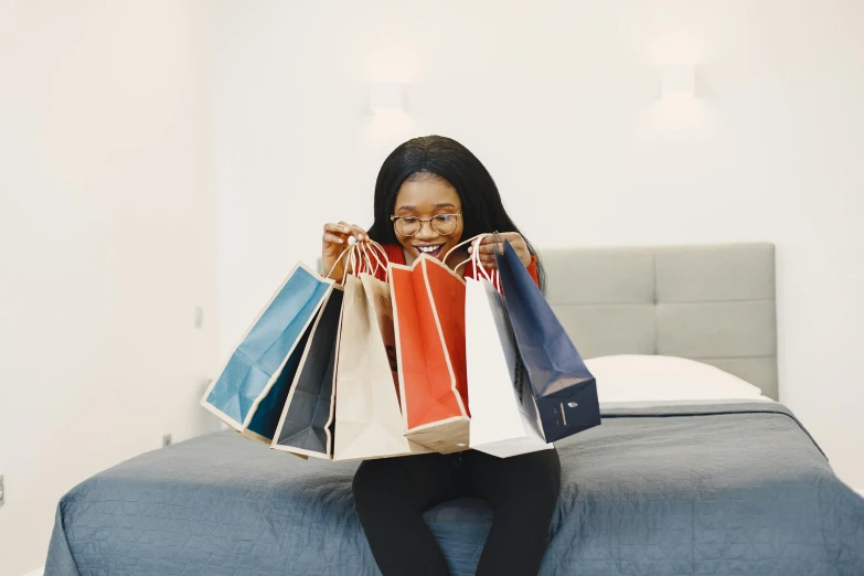 young woman sitting on bed with shopping bags