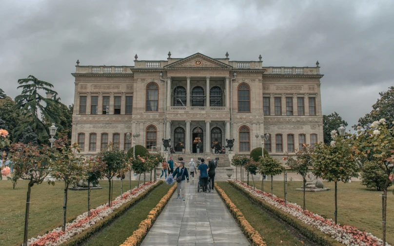 people walk towards a huge mansion sitting under cloudy skies