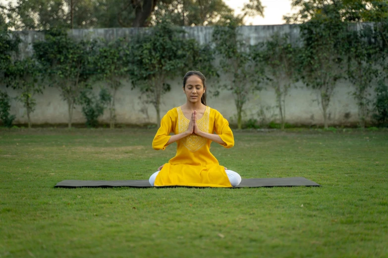 a woman in yellow outfit sitting on yoga mat doing yoga