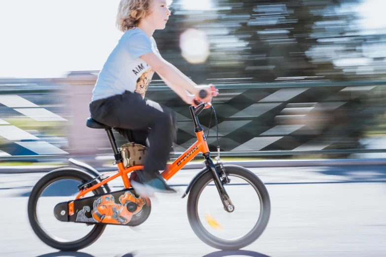 a boy rides his orange bike on the sidewalk