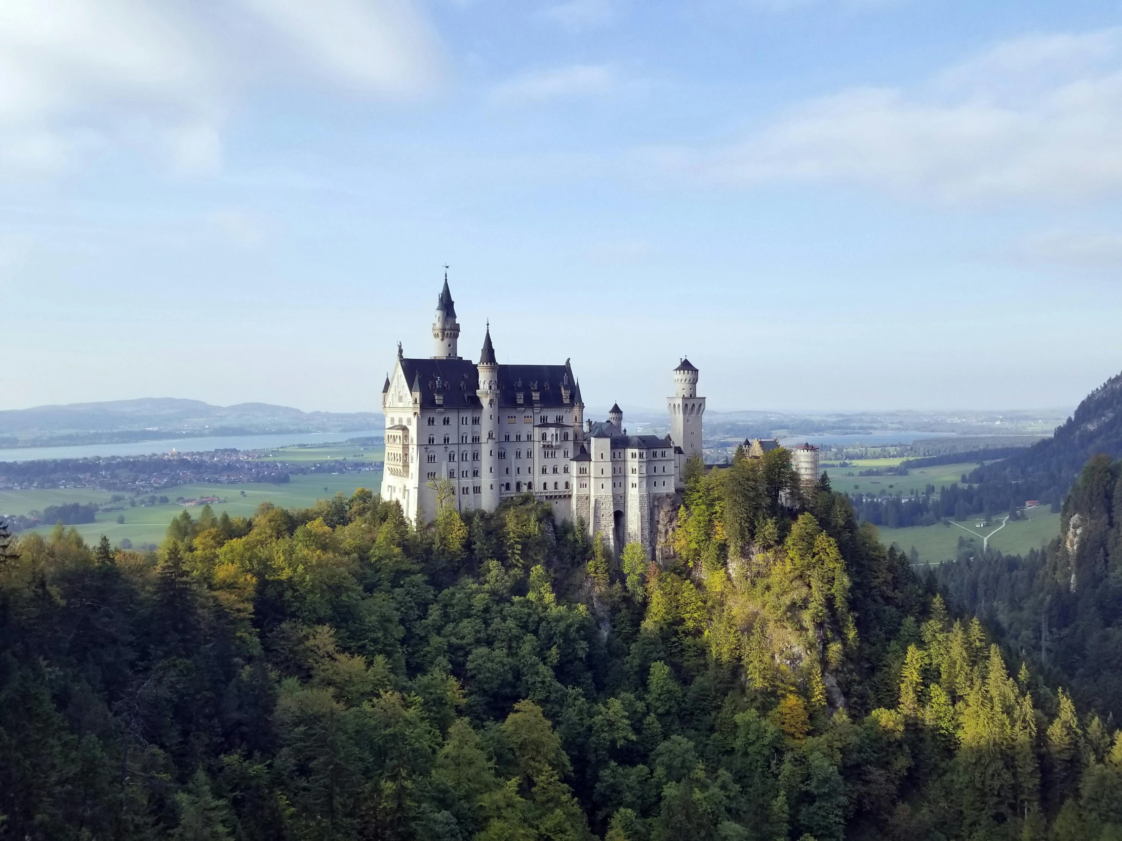 a castle perched on a large hill with a forest below