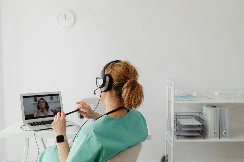 woman with headphones sitting at computer looking at a laptop