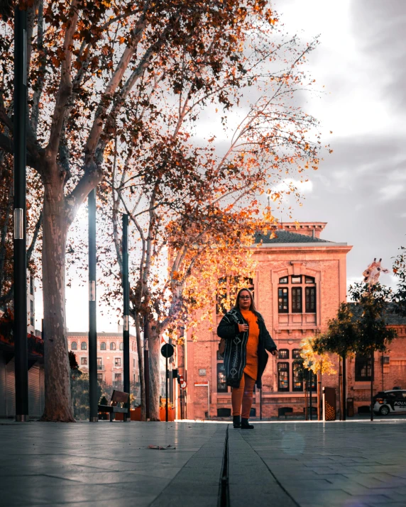 woman standing on a city sidewalk next to a tree with leaves