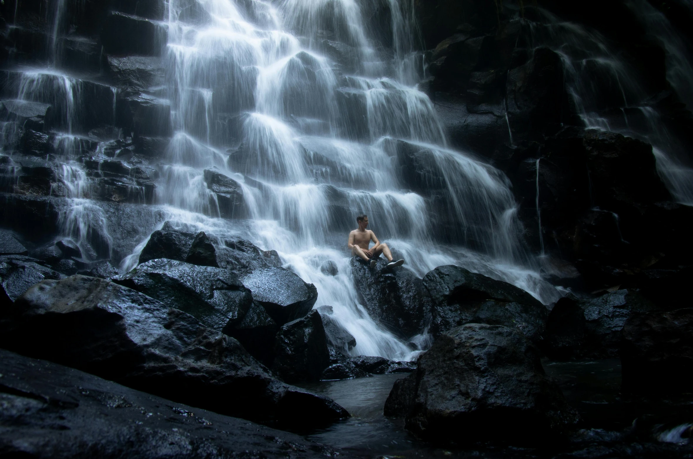 a young man sits in the middle of a waterfall