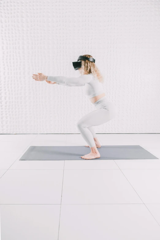 a woman in white leggings and black blindfold standing on a mat