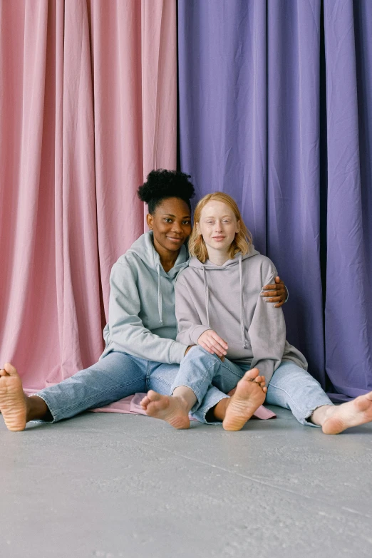 two girls sitting on the floor beside pink curtains