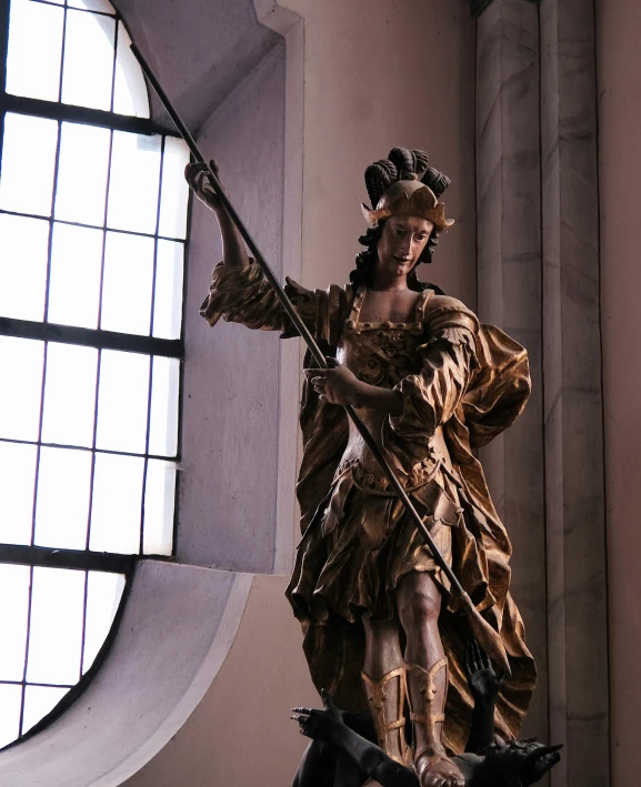a sculpture of a woman holding a spear next to windows