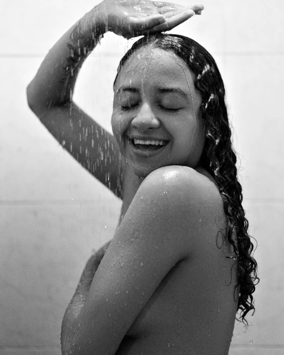 the girl smiles while holding the shower head up above her head