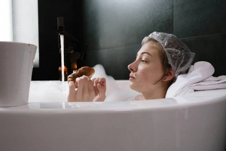 woman sitting on a tub in white bubble bath with a glass of water