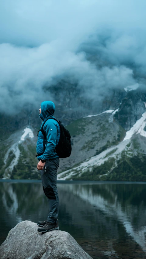 a man with backpack standing on rock next to large mountain