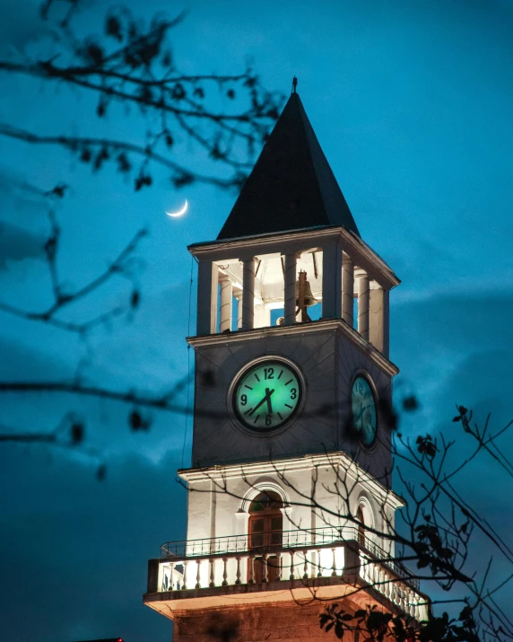 the clock tower has a full moon in the distance