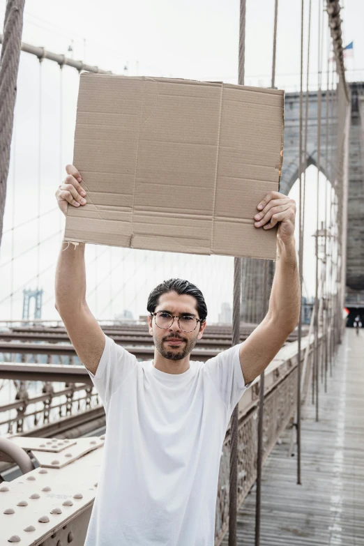 a man standing on a bridge holding up a brown sign