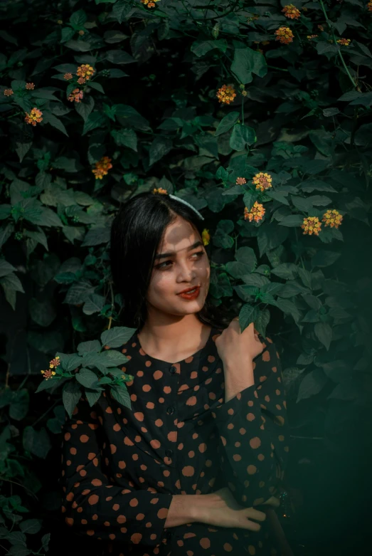 a woman standing between green leaves and yellow flowers