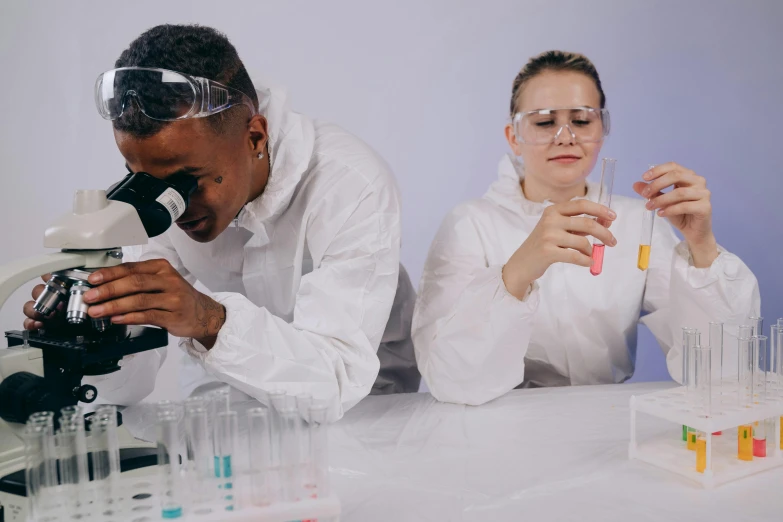 a man and a woman wearing protective glasses, holding a microscope and looking at soing through a pipe