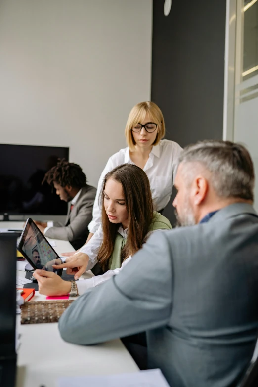 a group of people sitting around a desk looking at soing on a tablet