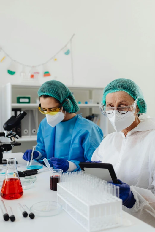 two people in blue robes and white cap work on laboratory equipment