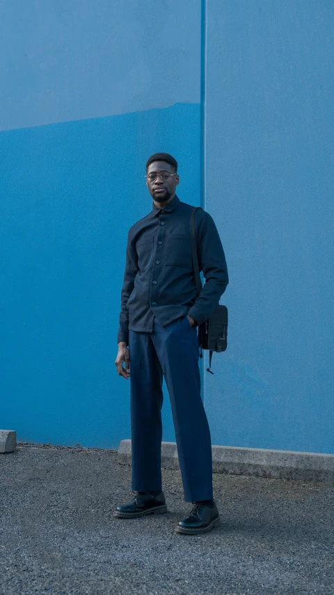 a man with sunglasses stands in front of a blue wall