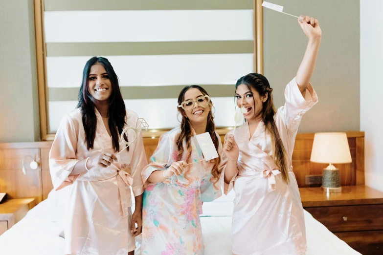 three women in robes smiling and waving with one of them holding up an item