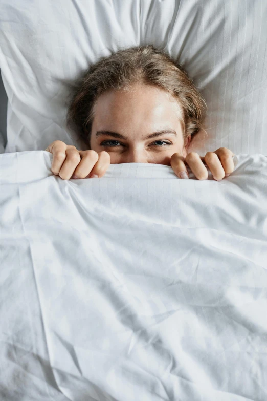 a beautiful young woman hiding behind white sheet