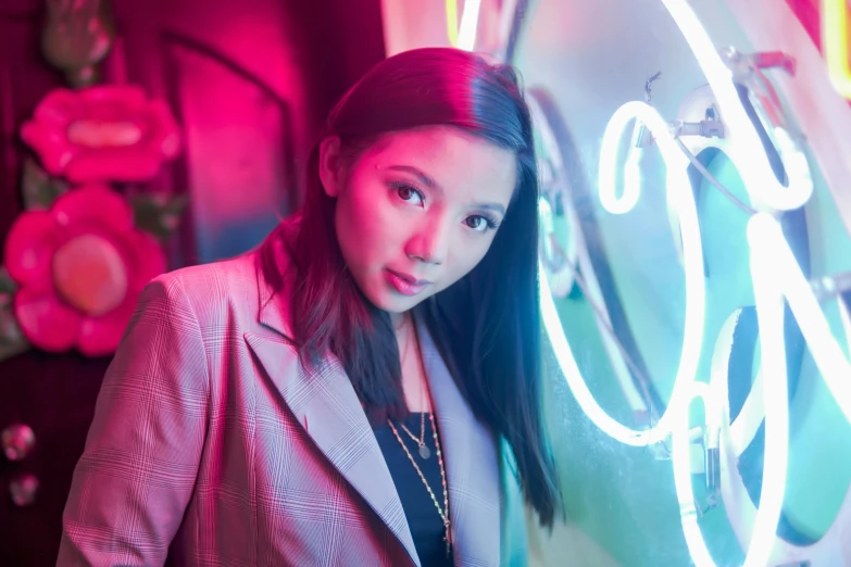 a young woman is standing in front of a neon light