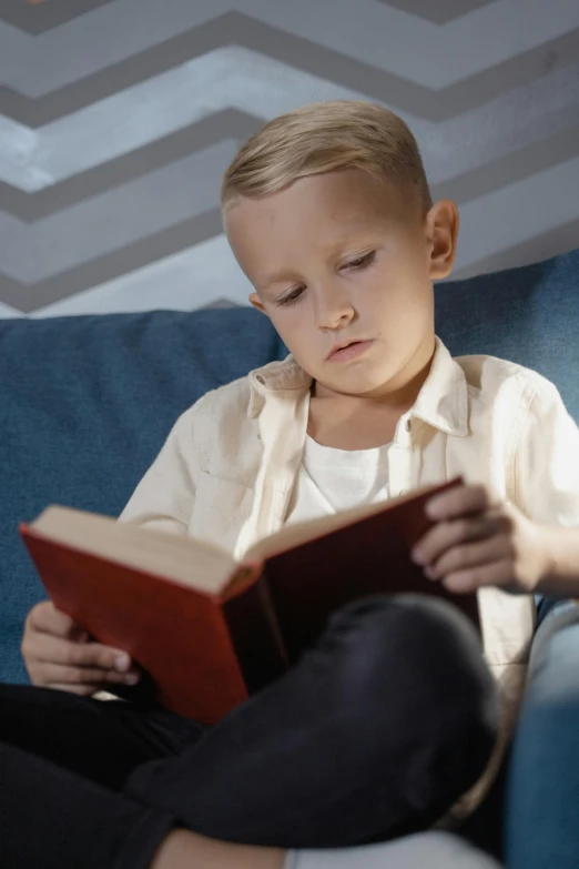 a small boy sits on the couch reading a book