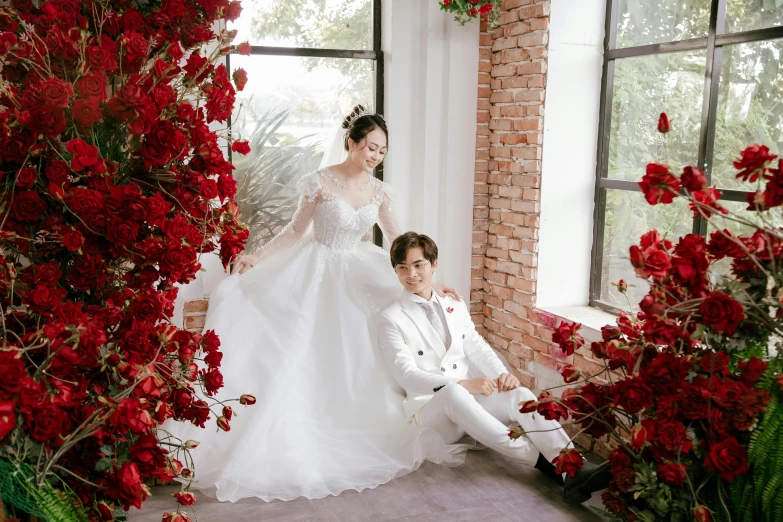an asian couple in wedding attire posing for a po in front of the window