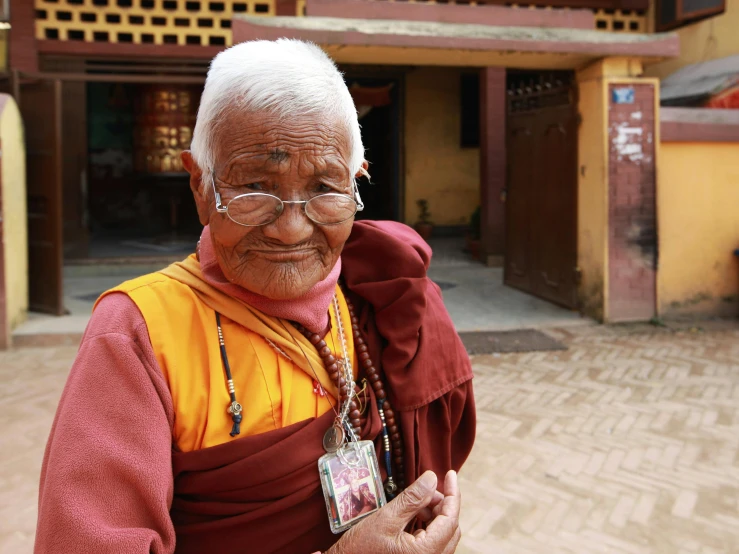 an elderly man wearing glasses and a red robe standing outside