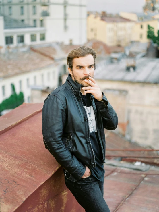 a man with dark hair and beard standing on a rooftop