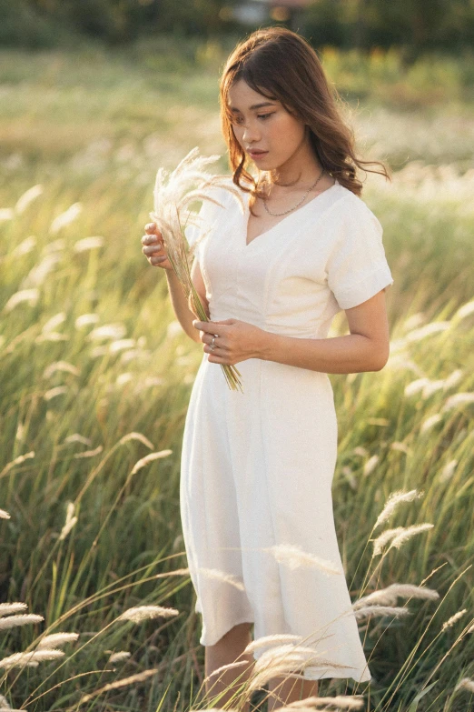 a young woman standing in the middle of a field holding a flower
