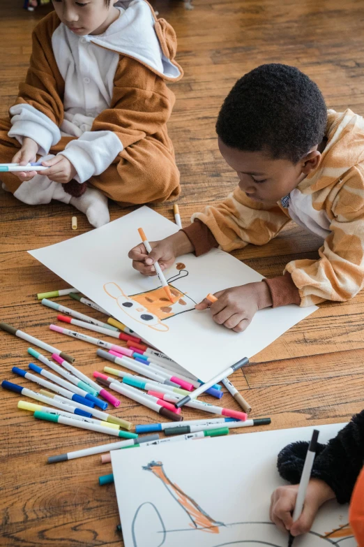 two young children are laying on the floor drawing