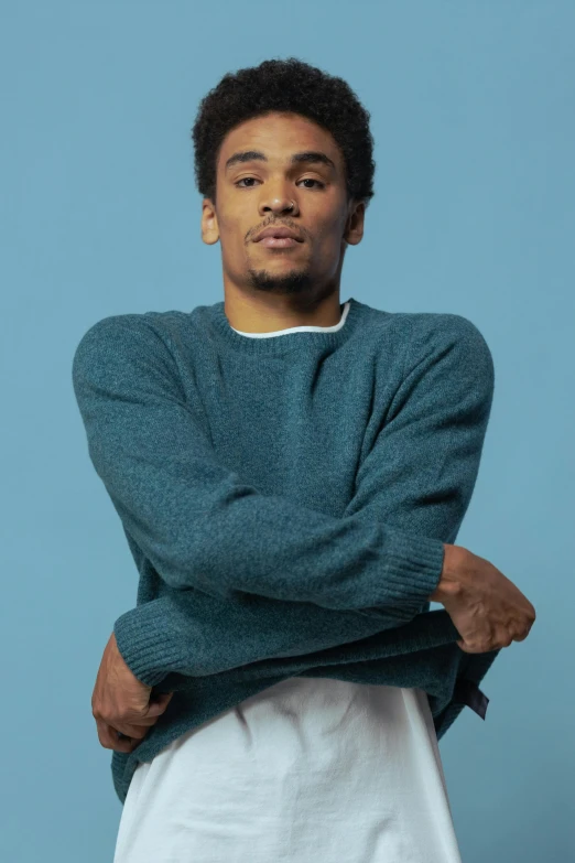 young man wearing a sweater is posing with his arms folded