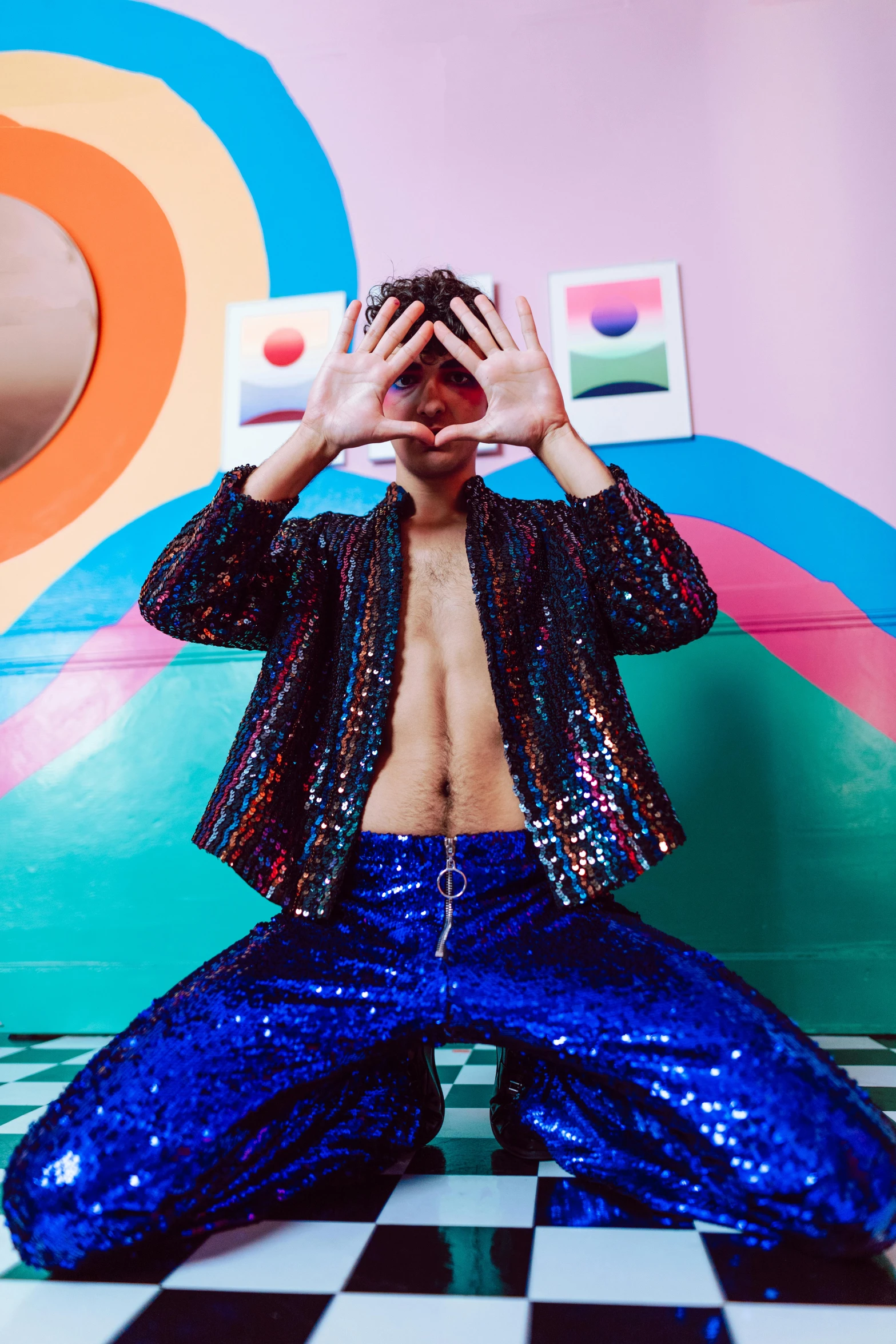 a man with blue pants and blue glitter sitting in front of a colorful wall