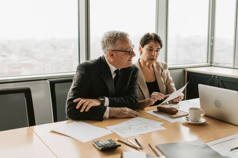 the two businessmen are sitting at a wooden table looking at papers