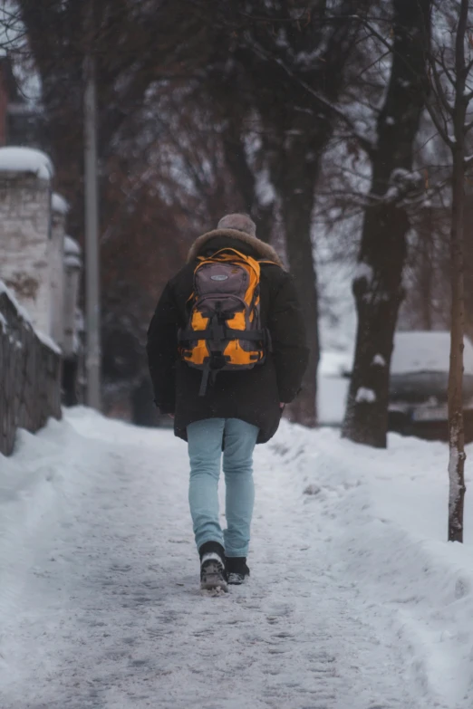 a person with a backpack and blue jeans walks down the snow covered road