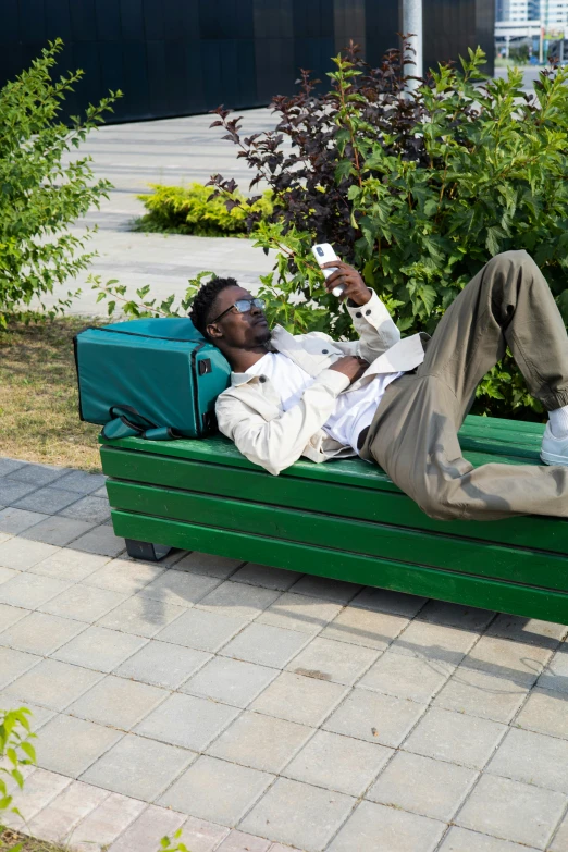 a person lying on a green bench holding up a camera
